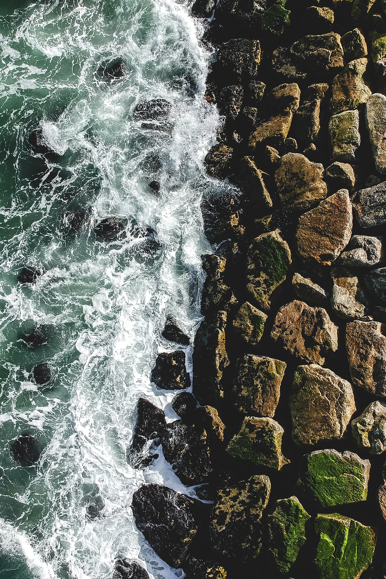 Blick von oben auf Wellen, die an eine aufgeschüttete Felsmauer prallen - Symbolbild für Quality Investing.