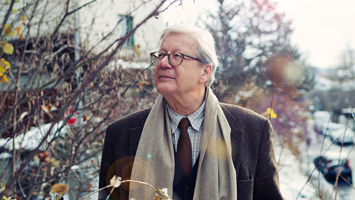 Outdoor shot with autumnal branches in the fore- and background. Georg Kohler with glasses, tie and loose scarf