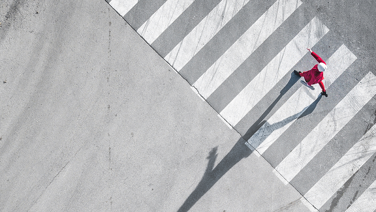 Aerial view of a single person on an empty street in an international city. The sun casts the shadow of an oversized human silhouette on the street.