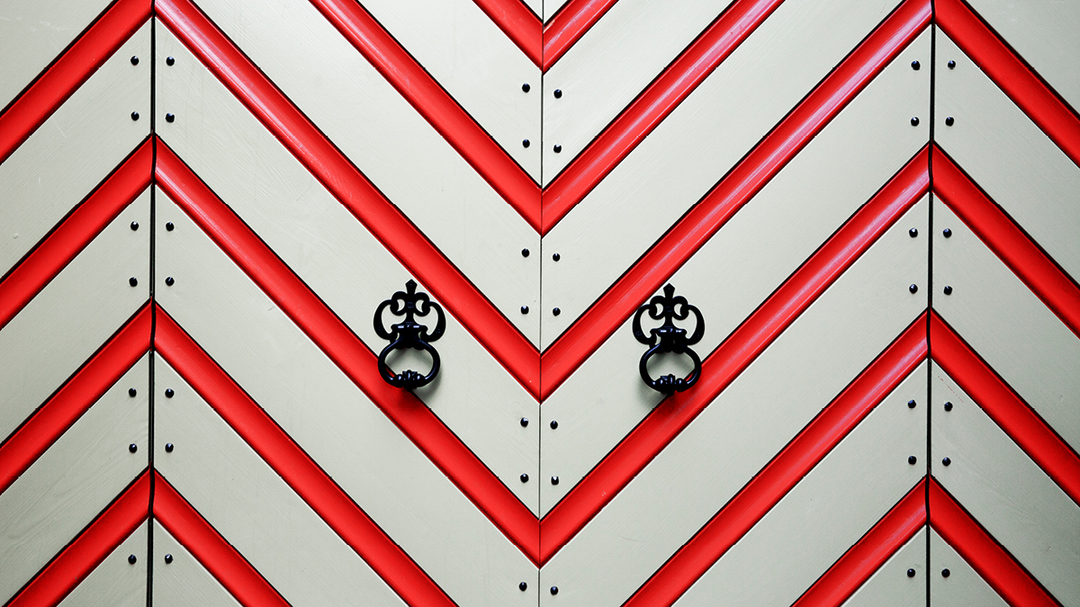 Close-up of a medieval gate. It is painted in a red and white zigzag pattern and decorated with nails.