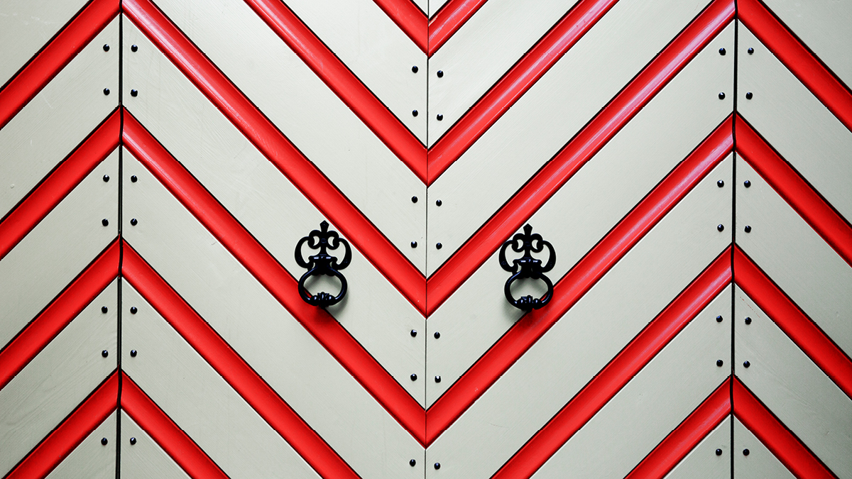 Close-up of a medieval gate. It is painted in a red and white zigzag pattern and decorated with nails.
